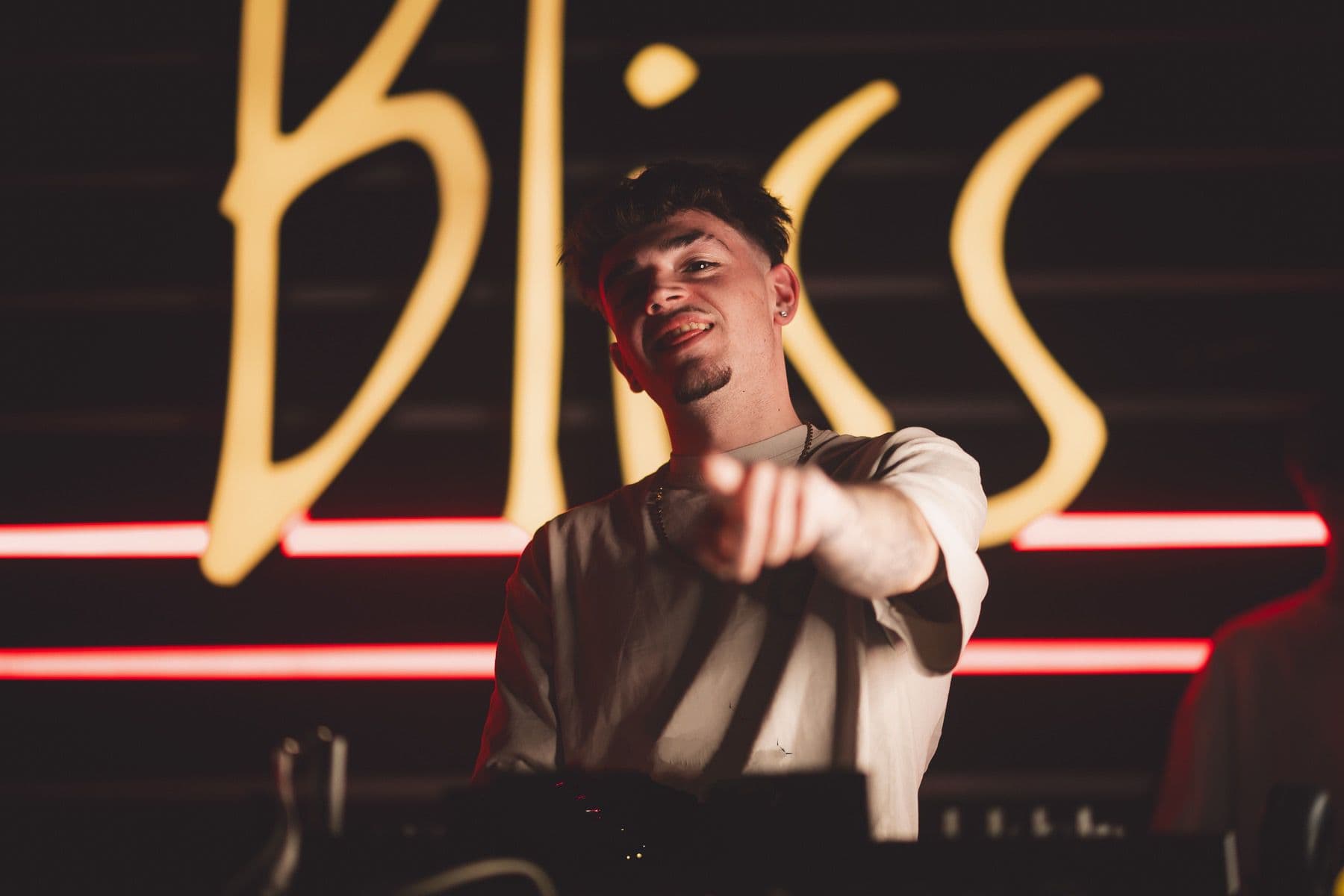 DjNotes senalando a camara frente a un fondo neon