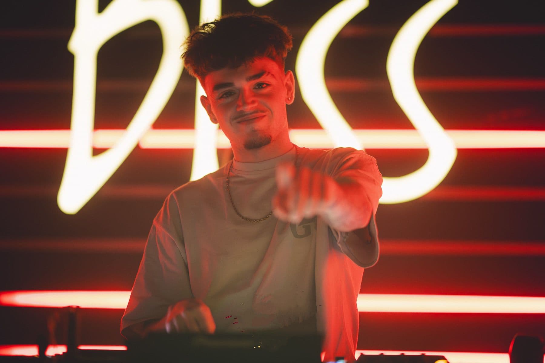 DjNotes senalando a camara frente a un fondo neon